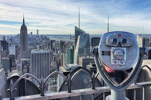 Une vue panoramique d’une ville avec ses imposants gratte-ciel, dont une flèche distinctive, observée à travers un télescope de style ancien.