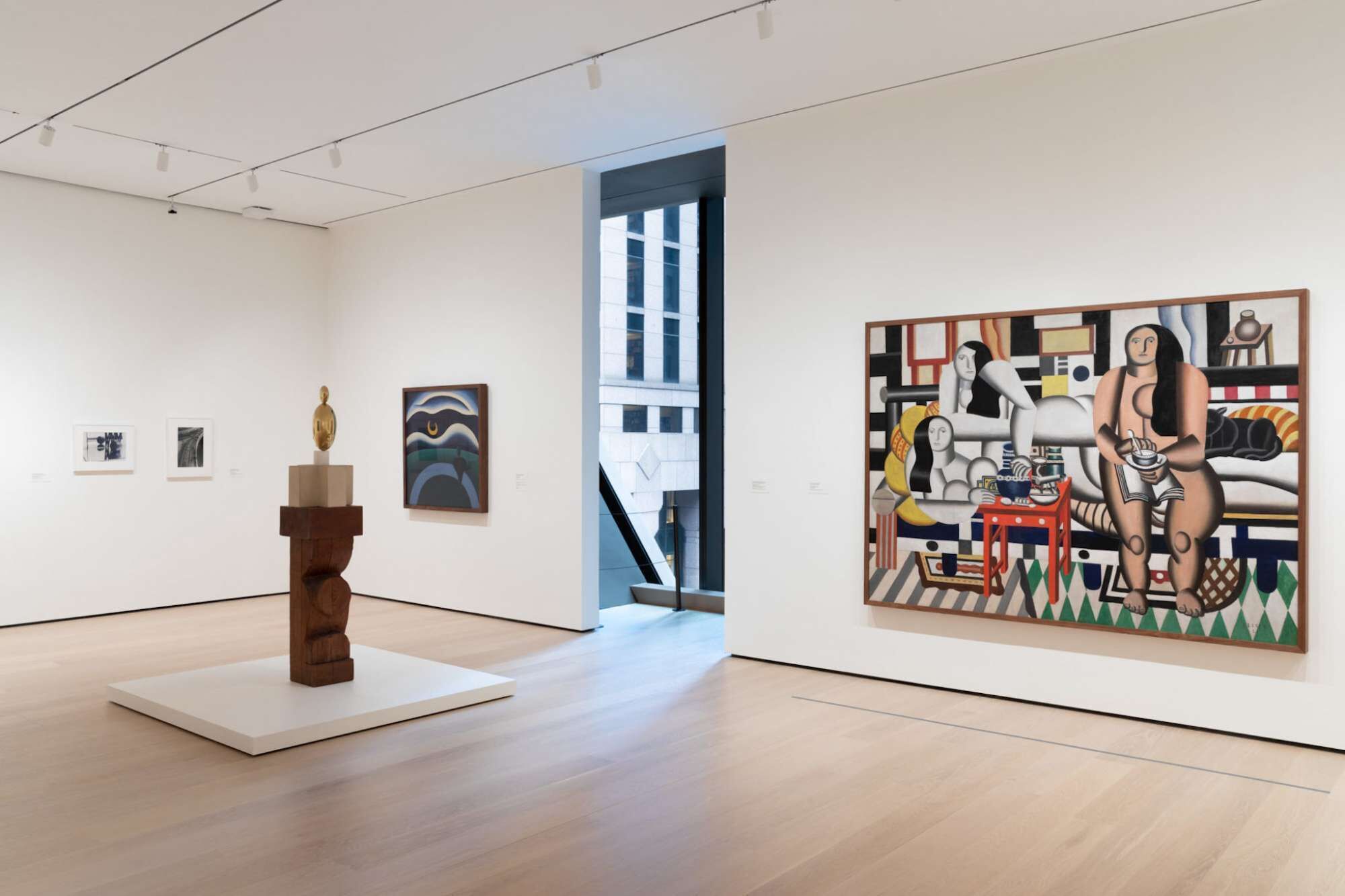 Une galerie d’art au décor moderne, où l’on peut admirer une sculpture en bois posée sur un piédestal et une grande peinture accrochée au mur.