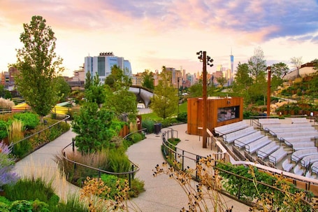 A rooftop garden with seating areas and a small wooden structure, surrounded by greenery and overlooking a cityscape.