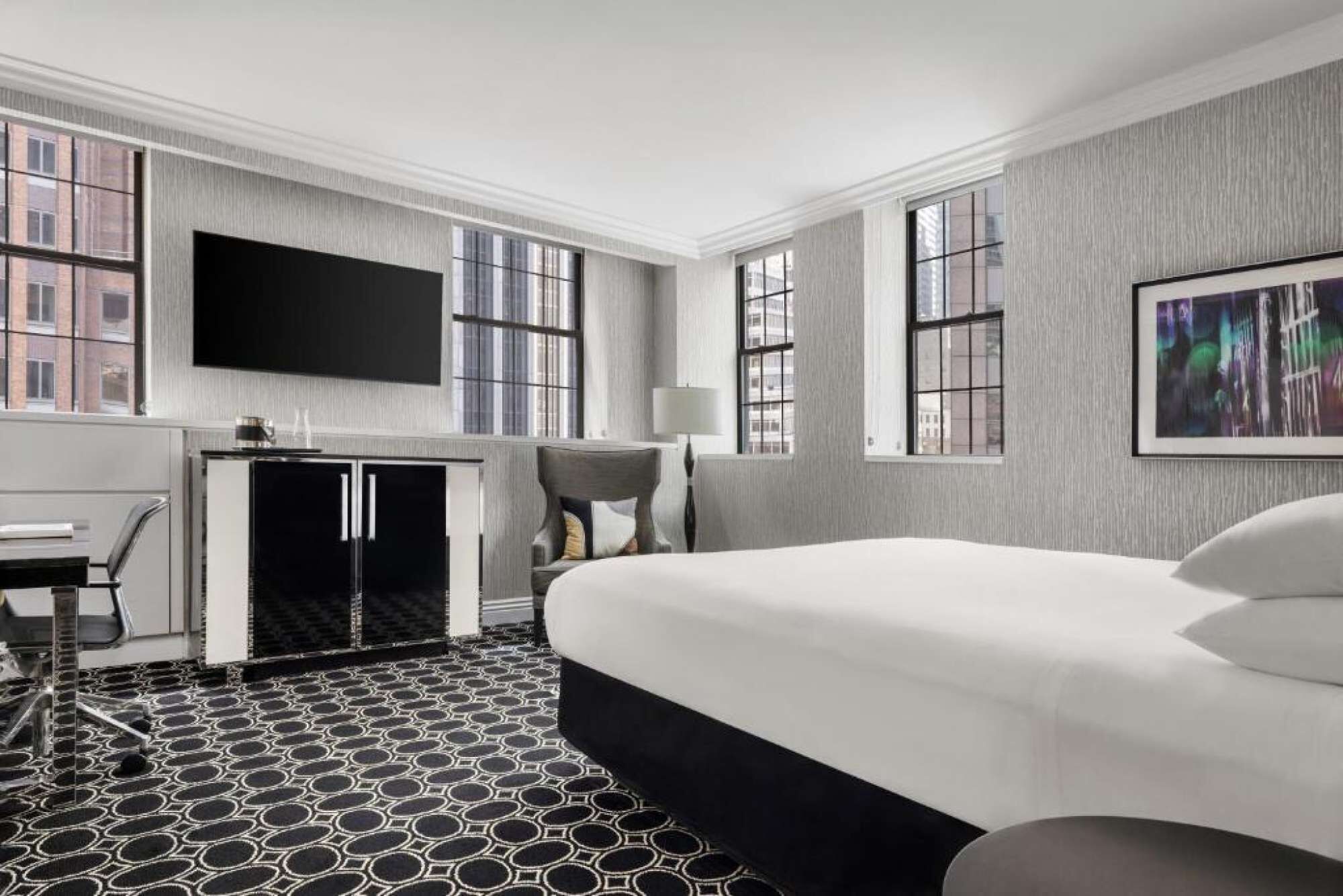 Una habitación de hotel con cama, escritorio, silla, televisión y ventana.