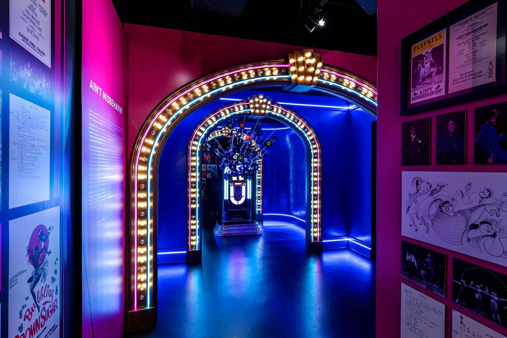 A brightly lit hallway with a neon archway and posters on the walls.