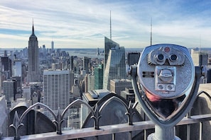Vista panorámica de un paisaje urbano con imponentes rascacielos, incluyendo una aguja distintiva, vista a través de un telescopio de estilo antiguo.