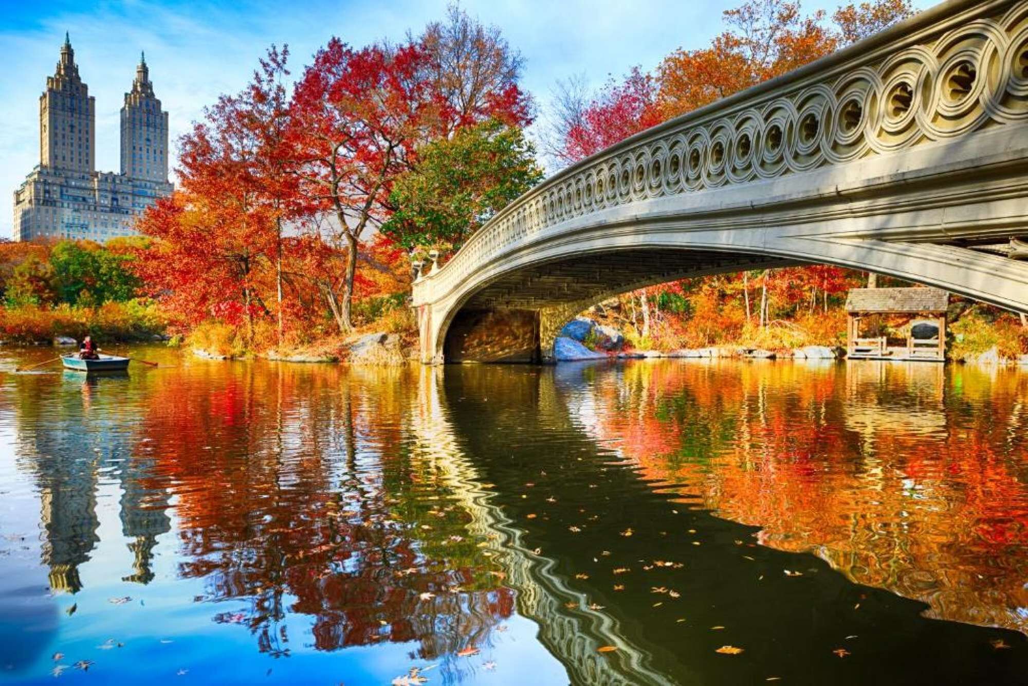Un pont de pierre enjambant une rivière, avec des arbres aux couleurs automnales et des bâtiments en arrière-plan.