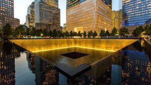 Una plaza urbana moderna con una fuente reflectante y edificios altos a su alrededor.