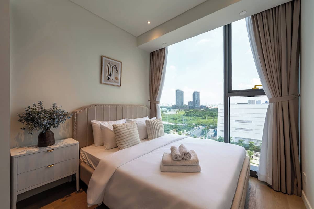Moderni hotellihuone, jossa on suuri sänky, yöpöytä, maljakko kukkineen ja näkymä kaupunkiin.