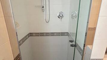 Un'area doccia vetrata con soffione e comandi, pareti piastrellate con una fascia decorativa e una porta in vetro.