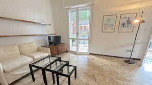 A living room with a sofa, a glass-top coffee table, a TV on a wooden cabinet, and a floor lamp. - Prioli First Floor Flexrent Abyssinia (Riccione)