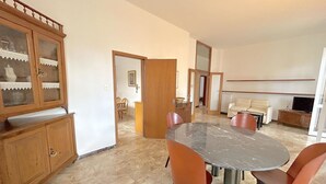 A dining area with a marble table and orange chairs, a wooden cabinet with glass doors, and a sofa in the background. - Prioli First Floor Flexrent Abyssinia (Riccione)