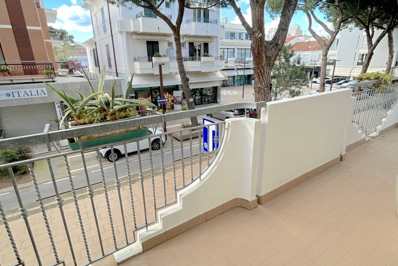 Un balcon doté d’une rambarde en métal donnant sur une rue où sont garées des voitures, et sur un immeuble sur lequel on peut lire l’inscription « ITALIA ».