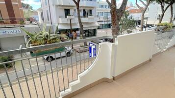 Un balcon doté d’une rambarde en métal donnant sur une rue où sont garées des voitures, et sur un immeuble sur lequel on peut lire l’inscription « ITALIA ».