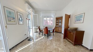 A spacious room with a marble floor, a dining area with a table and chairs, and a wooden cabinet. - Prioli First Floor Flexrent Abyssinia (Riccione)