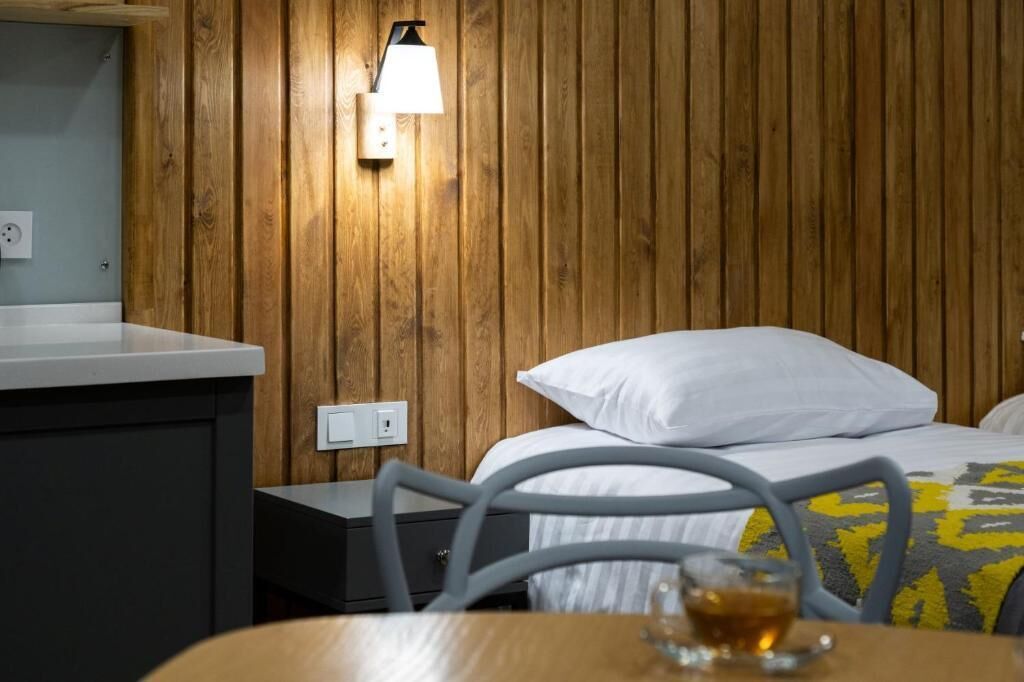 Une chambre d’hôtel avec un mur en bois, un lit avec une literie blanche, une table de chevet, une chaise et une lampe.