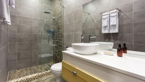 Un baño moderno con cabina de ducha de vidrio, un lavamanos blanco y un espejo con toallero.