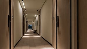 A long, narrow hallway with doors on both sides, recessed lighting, and a bench in the center. - Resort Cupidon Neptun (Neptun)