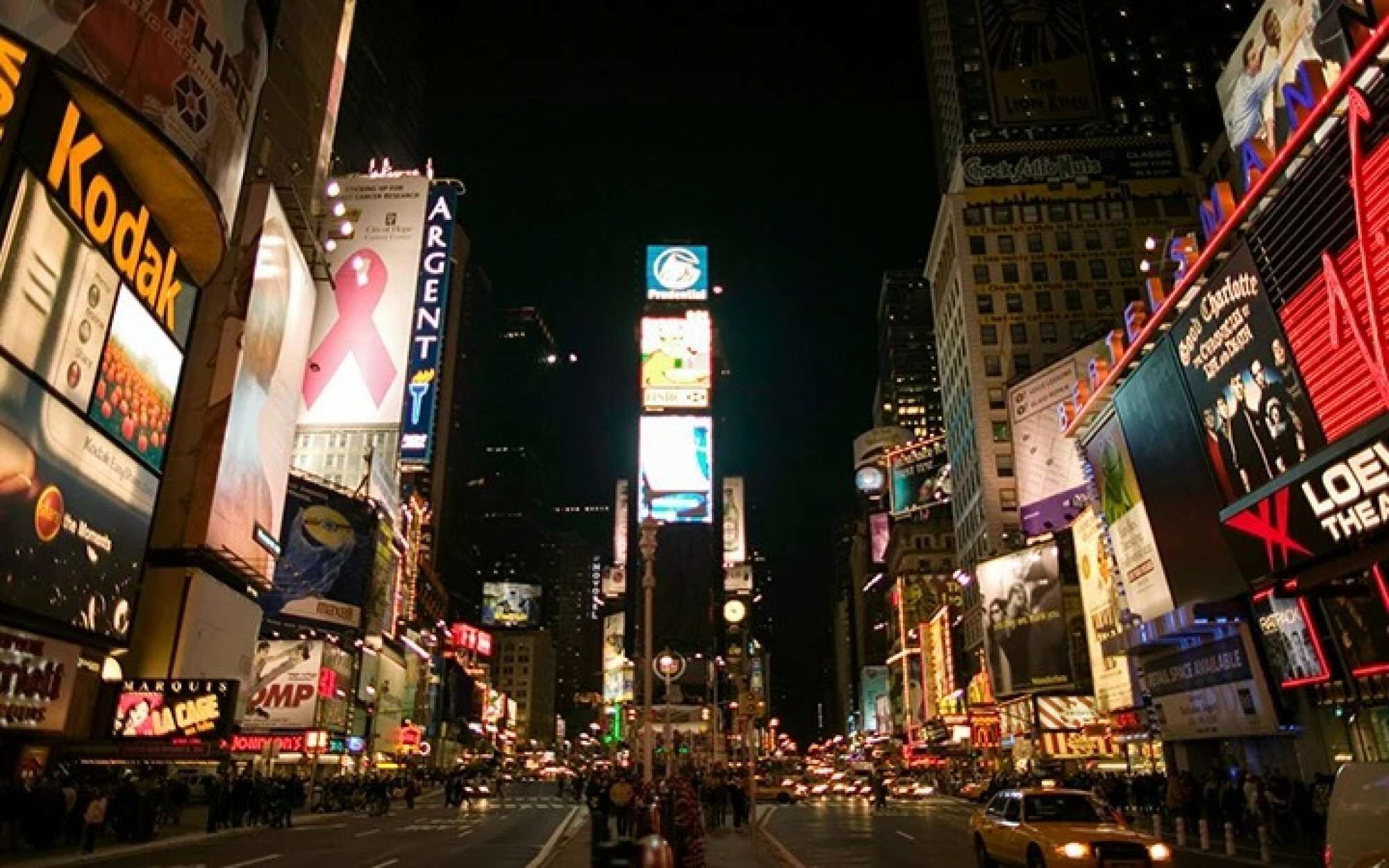 Una calle urbana concurrida de noche, con vallas publicitarias y carteles iluminados.
