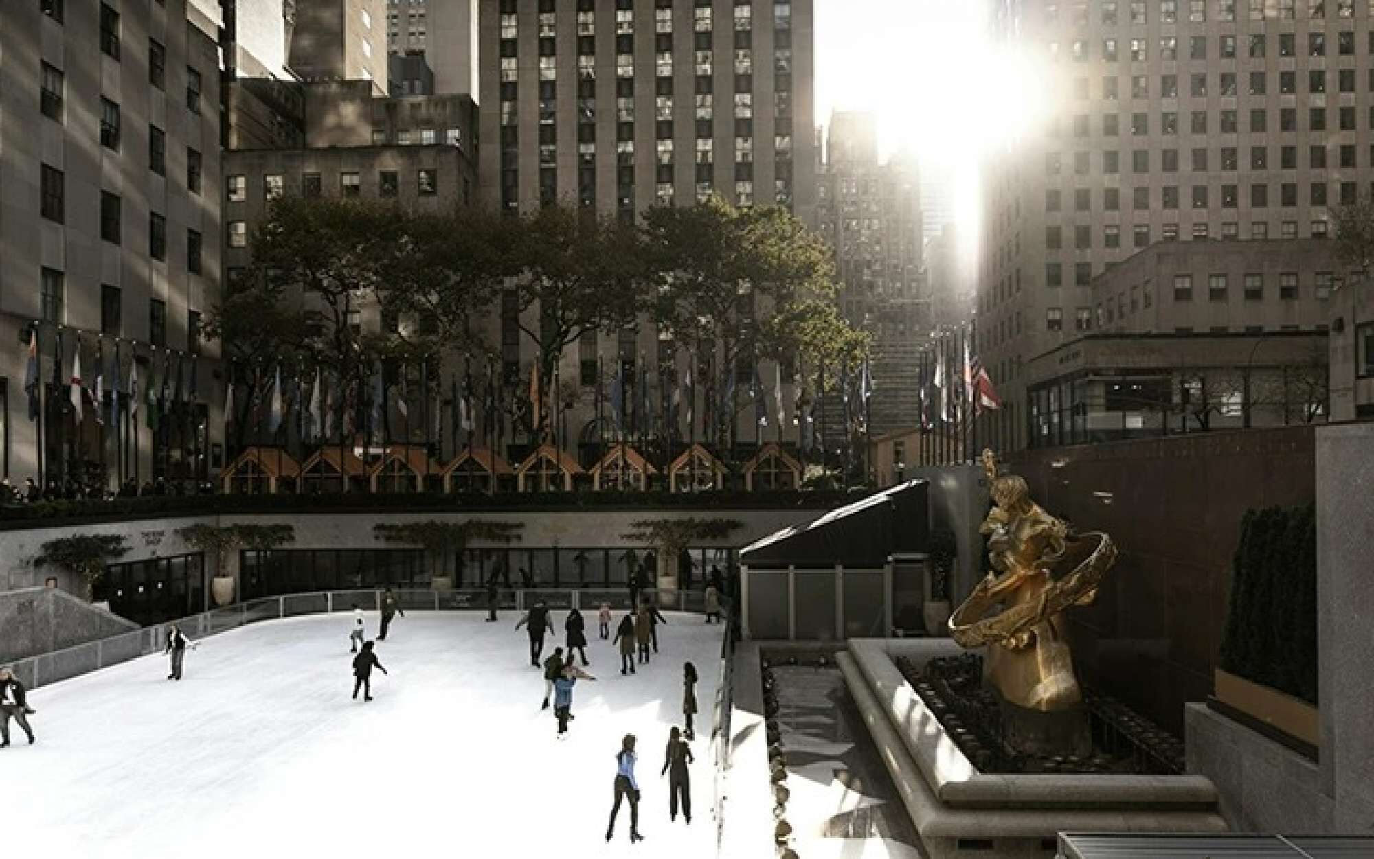 An outdoor plaza with a large fountain and a statue, surrounded by tall buildings.