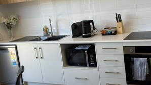 Ett modernt kök med vita skåp, en diskmaskin i rostfritt stål, en mikrovågsugn, en vattenkokare och ett diskho.