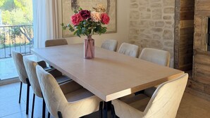Ein Essbereich mit einem langen Tisch, sechs Stühlen und einem Blumenstrauß. Eine Steinwand und eine Holzbalkendecke sind ebenfalls vorhanden.