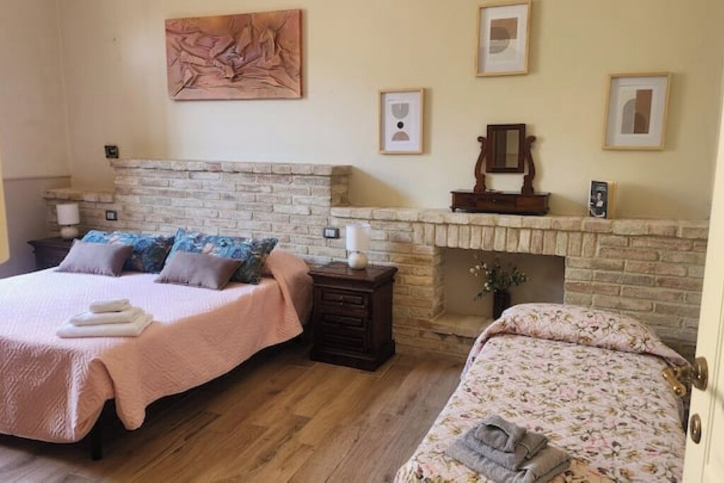 Ein Schlafzimmer mit zwei Betten, einem Steinkamin und gerahmten Kunstwerken an den Wänden.