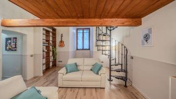 Un soggiorno con soffitto in legno, un divano, una scala e una libreria.