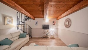 Una sala de estar con techo de madera, un conjunto de sofás, un televisor y una escalera.