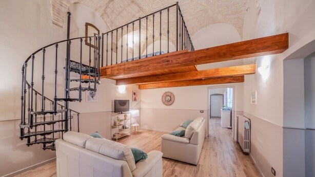 Amplia sala de estar con una escalera de madera, sofás blancos y un televisor.