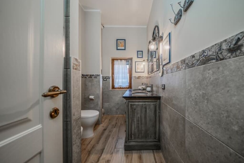 A narrow bathroom with a toilet, a wooden vanity, and a marble-tiled wall.