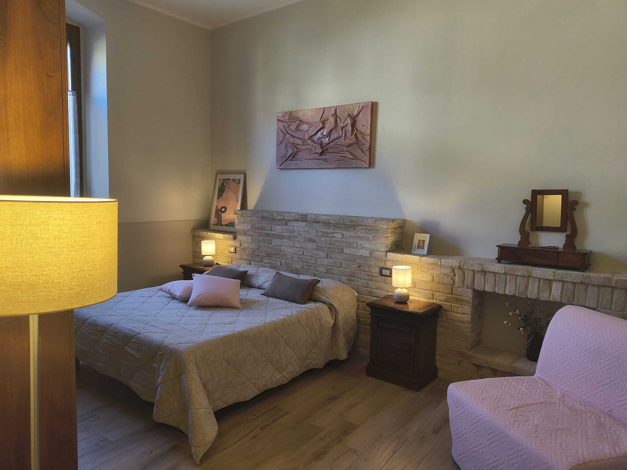 A bedroom with a bed, bedside tables, a fireplace, and a painting on the wall.
