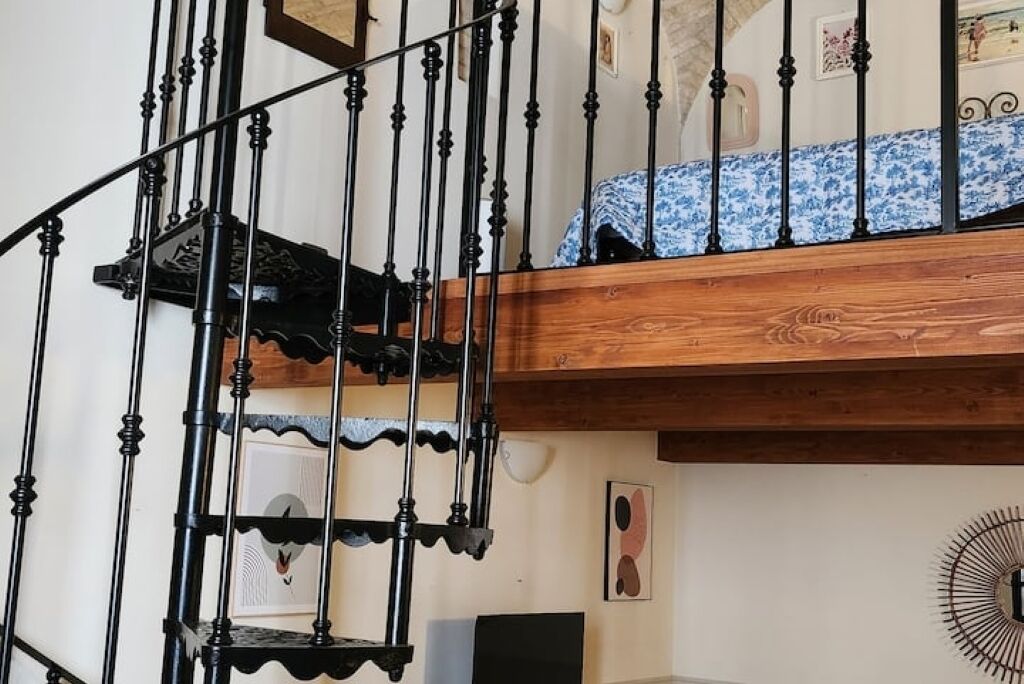 A spiral staircase with black balusters and a wooden handrail, leading to a balcony with a blue and white patterned cover.