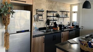 Una cocina moderna con electrodomésticos de acero inoxidable, armarios de madera y una lámpara colgante negra.