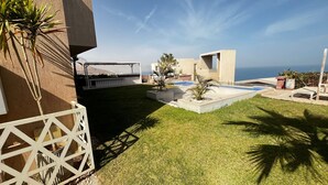 Un espacio exterior moderno con piscina, una pérgola y vistas al océano.