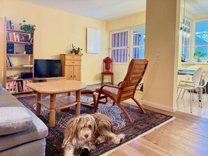 A living room with a wooden table, a television, a bookshelf, and a dog lying on a rug. - Claudis Seeland vacation apartment - Comfortable stay by the lake in Kressbronn (Kressbronn)