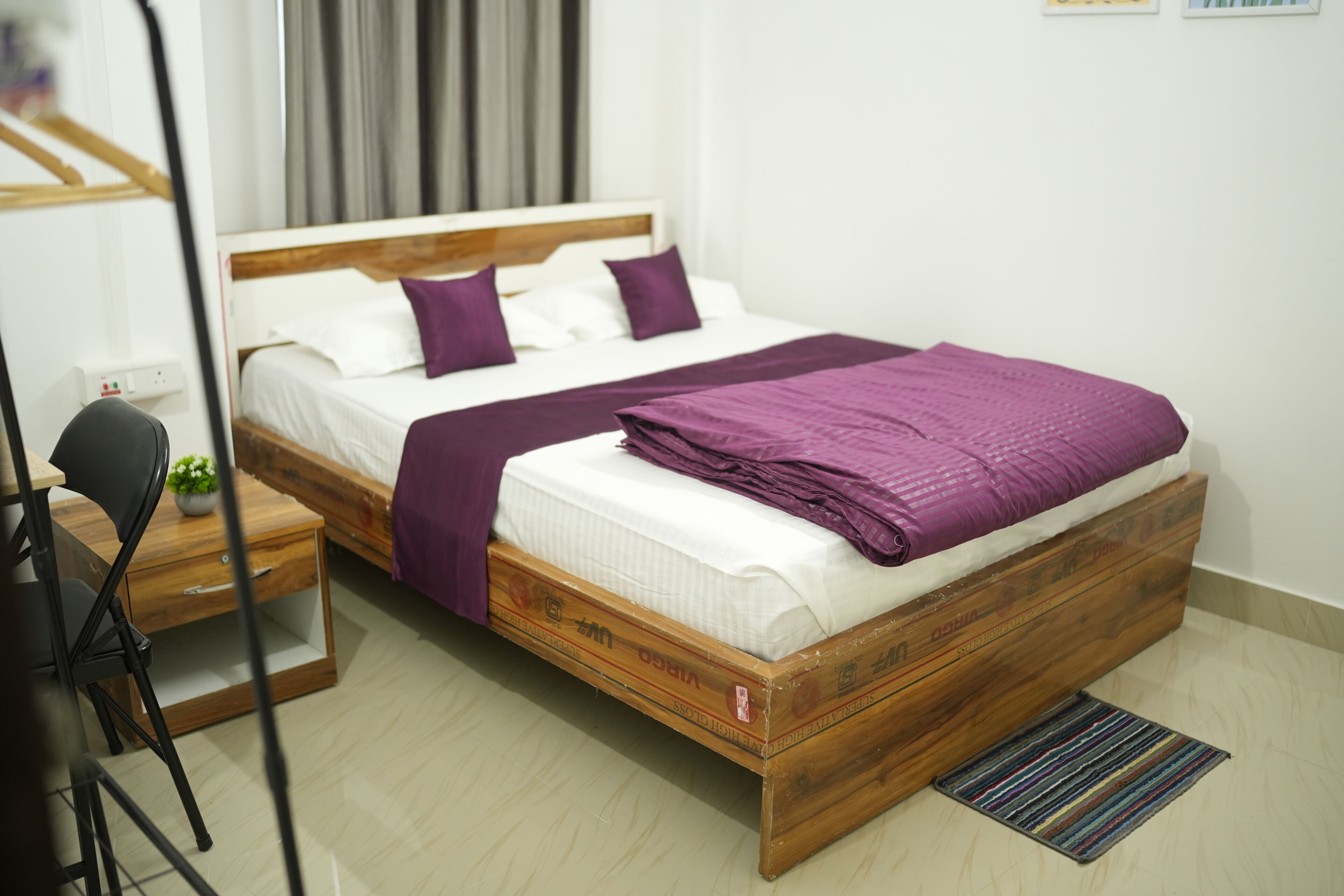 A single bed with a wooden frame, white bedding, and purple accents.