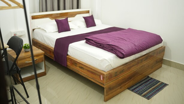 Un lit simple avec un cadre en bois, une literie blanche et des touches de couleur violette.
