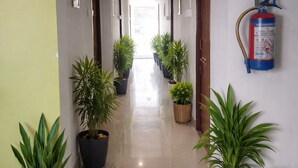 A hallway with potted plants, a fire extinguisher, and doors leading to rooms. - Shivalik stays  (East Jorhat)