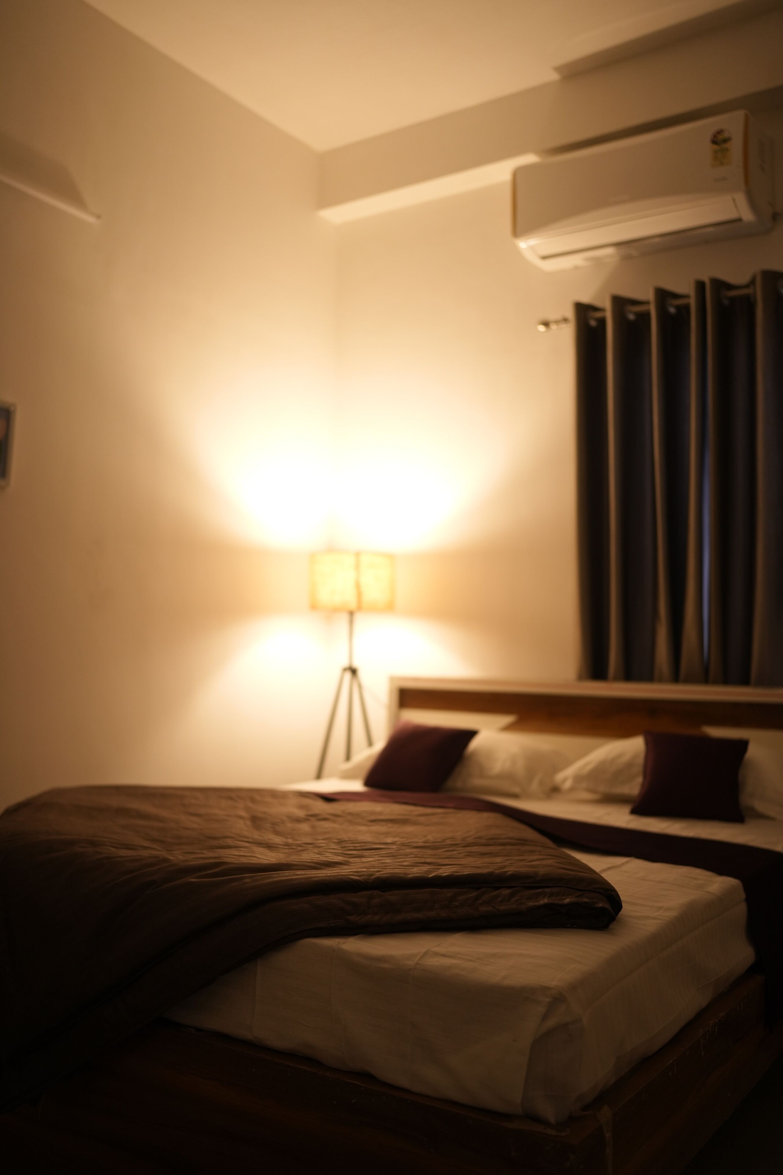 Habitació d'hotel amb llit, làmpada de nit, aire condicionat i cortines.