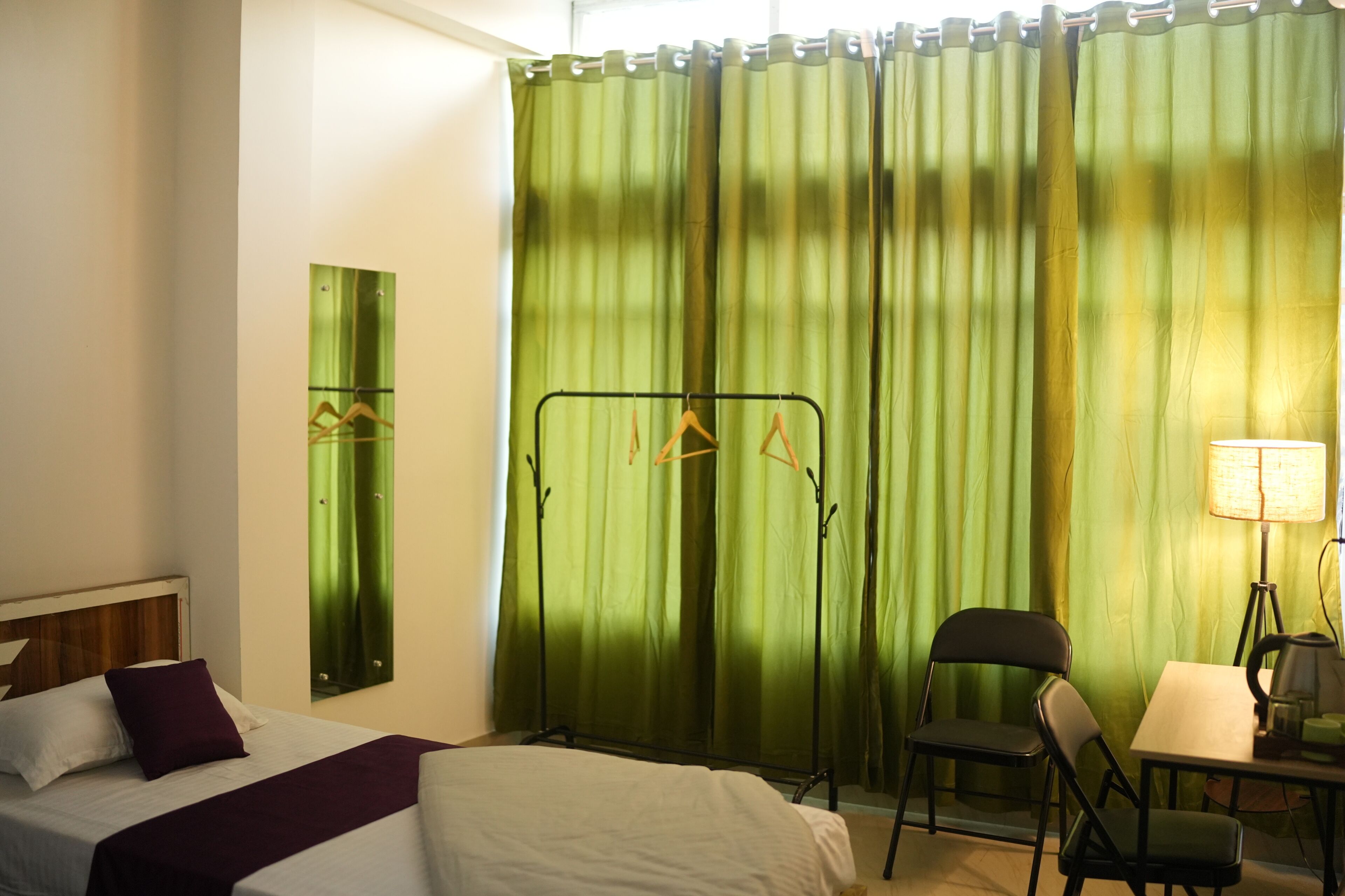 A hotel room with a bed, a desk, a chair, a lamp, and a curtain.