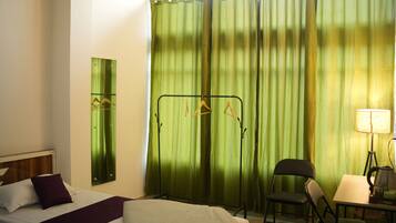A hotel room with a bed, a desk, a chair, a lamp, and a curtain.