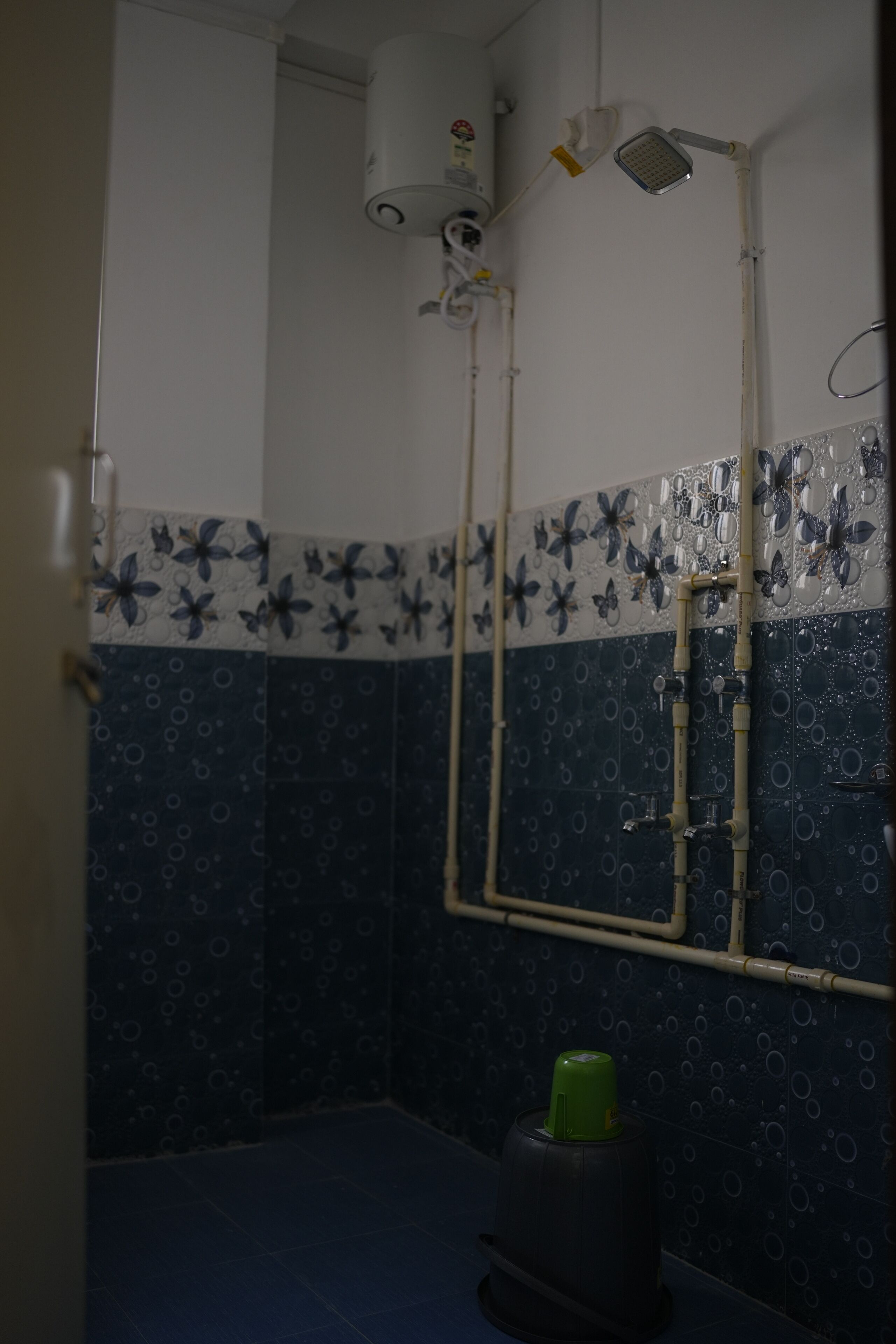 A bathroom with blue and white patterned tiles, a shower area with a green bottle, and a white ceiling with a showerhead.
