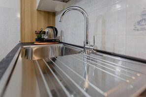 Ein Edelstahl-Spülbecken mit modernem Wasserhahn, eine Holzwandverkleidung und eine Kaffeemaschine auf der Arbeitsplatte.
