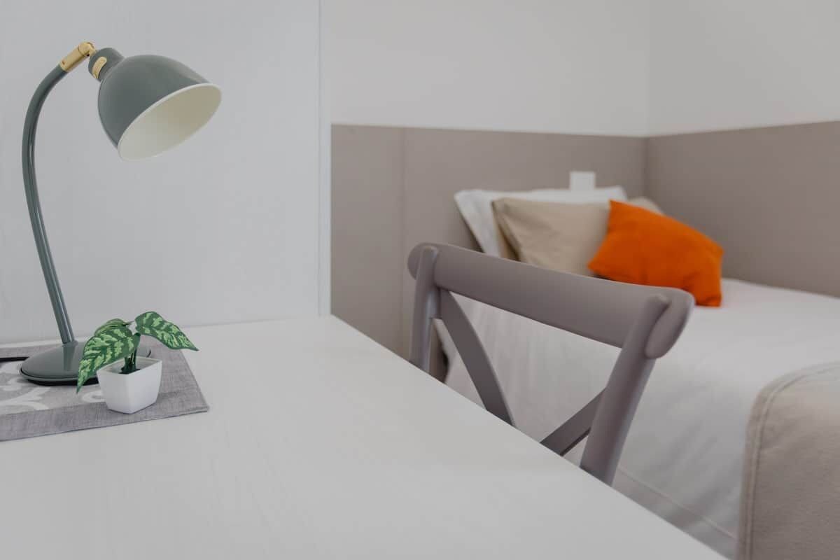 A neatly arranged room with a desk, chair, and a bed with pillows.