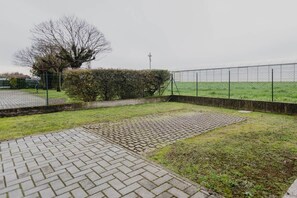Ein gepflasterter Außenbereich mit einem Ziegelweg, einer Rasenfläche und einem Metallzaun.