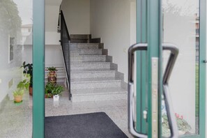 Eine Treppe führt zu einer oberen Etage, mit einem Glastür-Eingang und Blumentöpfen auf der Landung.