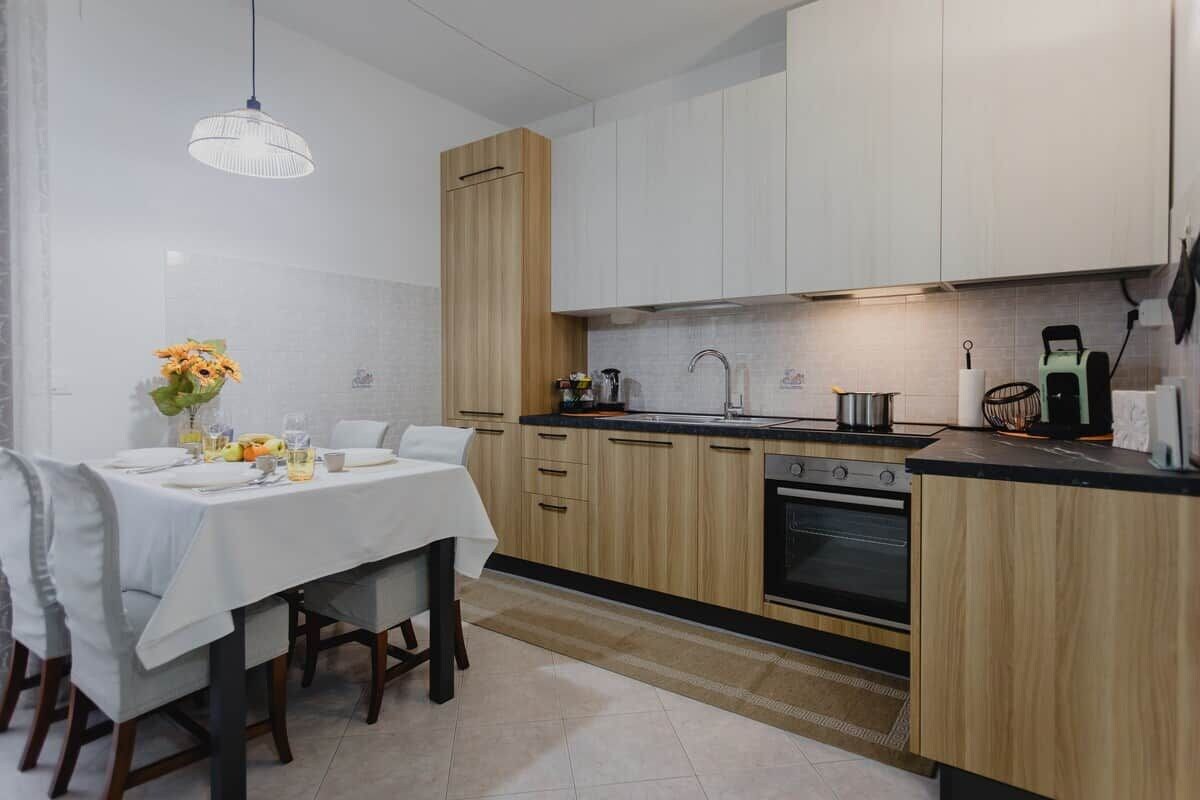 Une cuisine moderne avec des armoires blanches, un mur d’accent en bois, une table à manger avec des chaises et un luminaire suspendu.