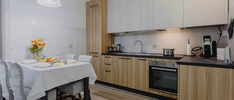 A modern kitchen with white cabinets, a wooden accent wall, a dining table set with chairs, and a hanging pendant light.
