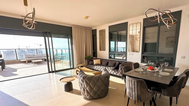 A modern living room with a dining area, large windows, and a view of the cityscape. - Sky26 Mini penthouse with 6-Rooms Sew View Bat Yam (Bat Yam)