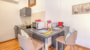 Eine kompakte Küche mit Mikrowelle, Toaster und Spüle. Zwei Stühle und ein kleiner Tisch mit Tellern und einer Blumenvase.