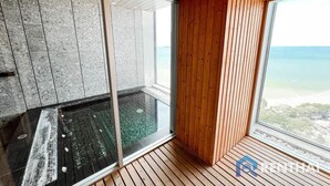 Ein modernes Zimmer mit Holzboden, einer Glastrennwand und Blick aufs Meer.