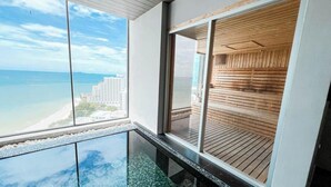 Ein Hotelzimmer in einem Hochhaus mit großem Balkon, einer Glasbodenkonstruktion und Blick auf Strand und Meer.