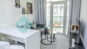 Une chambre d’hôtel moderne avec un bureau blanc, un canapé, une petite table ronde et un balcon avec une chaise.